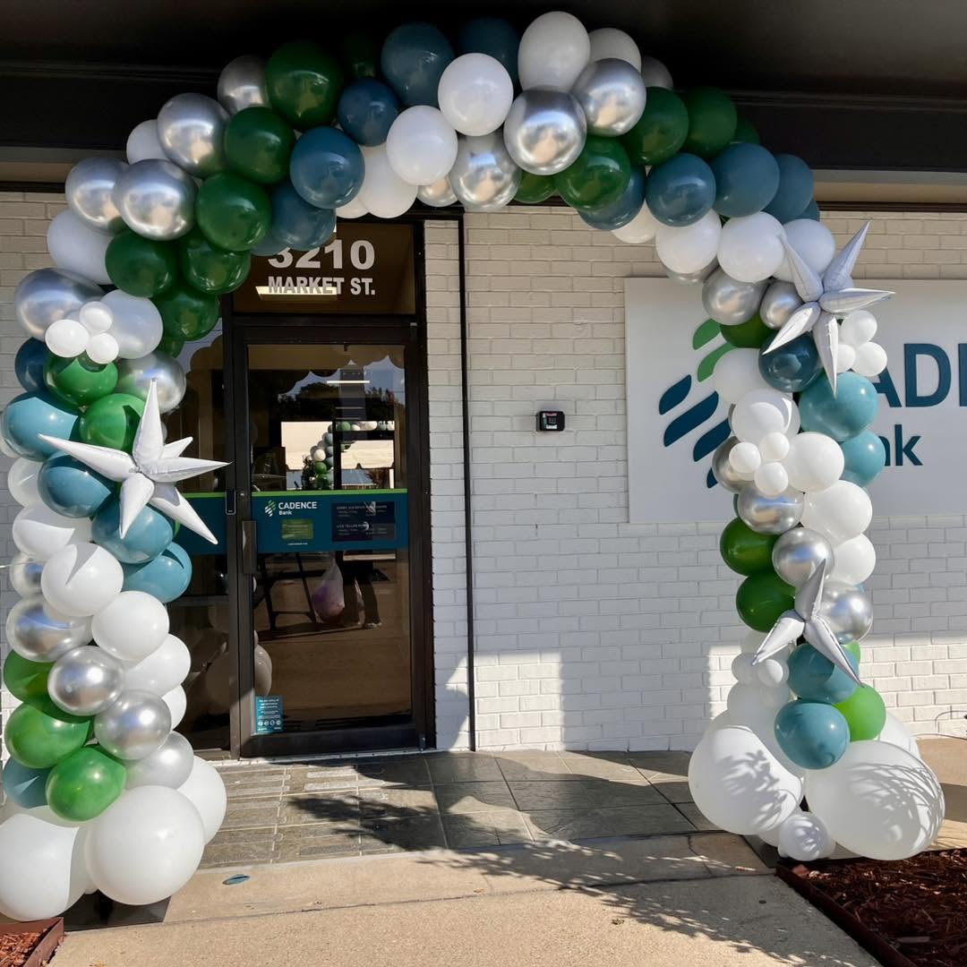 Green, teal, white and silver balloon arch over the Cadence Bank grand opening entrance