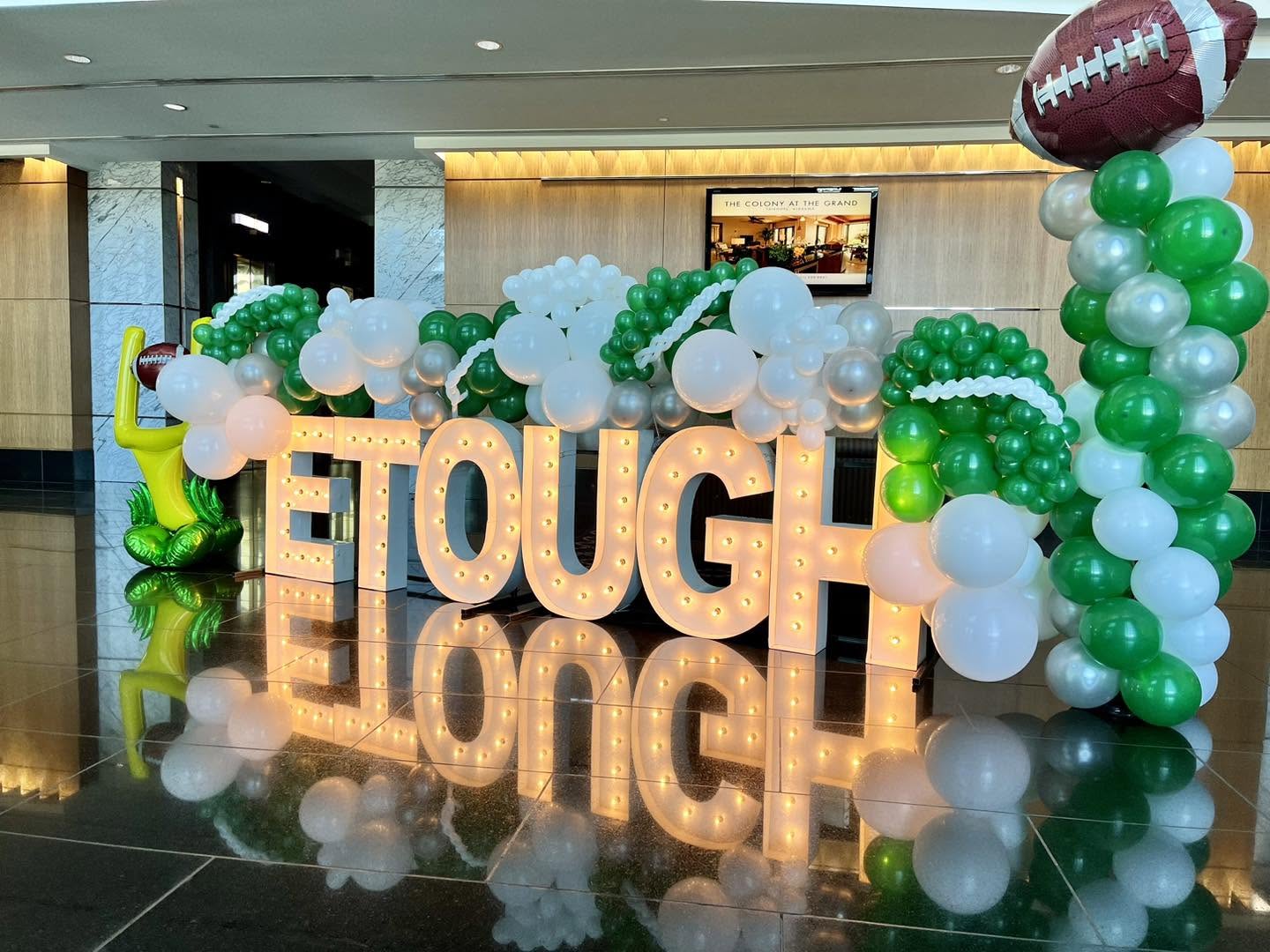 Illuminated marquee letters with green and white balloon décor in a polished lobby