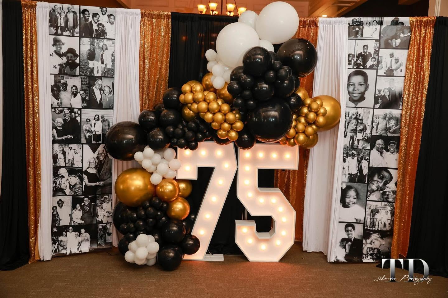 Black and gold 75th birthday marquee numbers with balloon garland and photo curtain backdrop