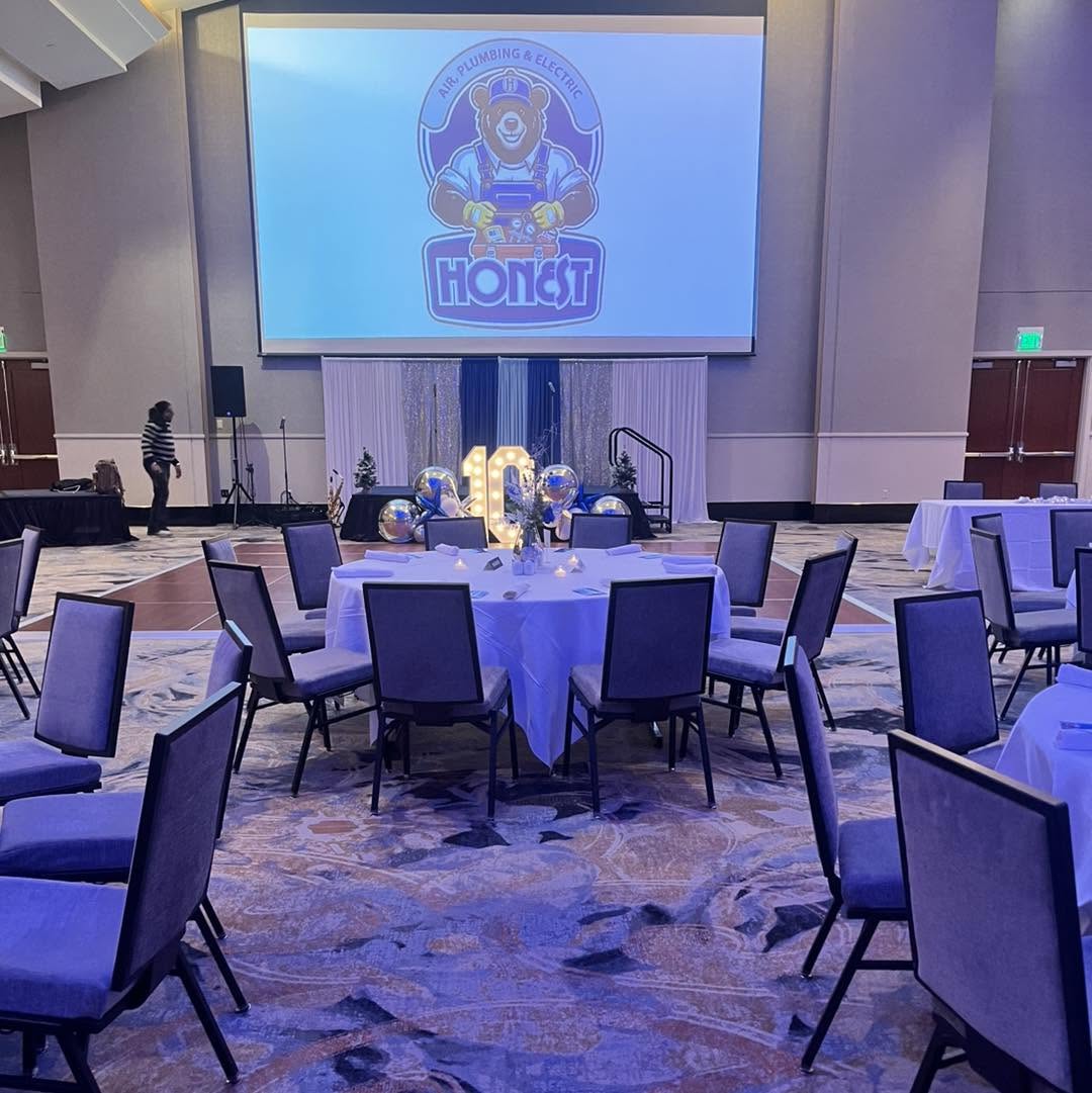 Ballroom reception with round tables facing a branded stage and marquee numbers