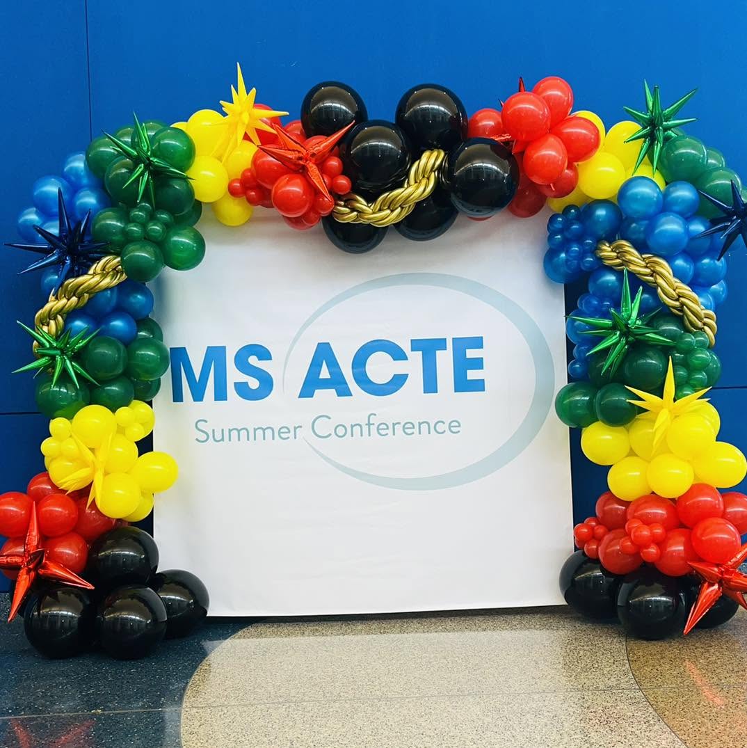 Bold red, yellow, green, blue and black balloon arch framing the MS ACTE Summer Conference backdrop