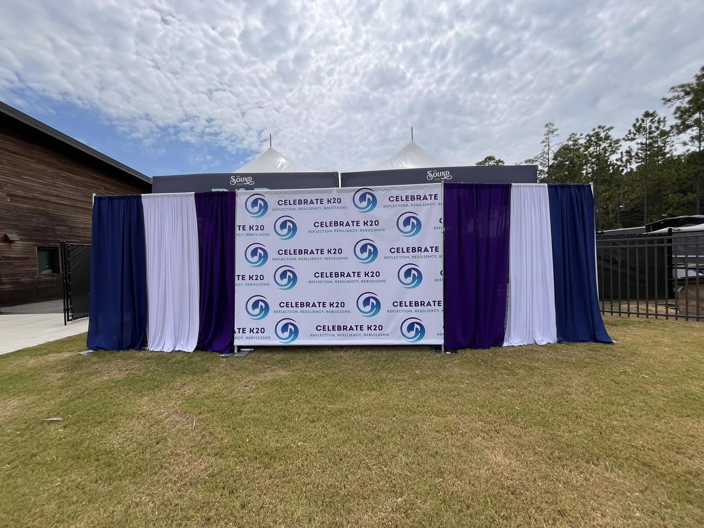 Celebrate K20 branded backdrop framed with navy, purple and white drape panels
