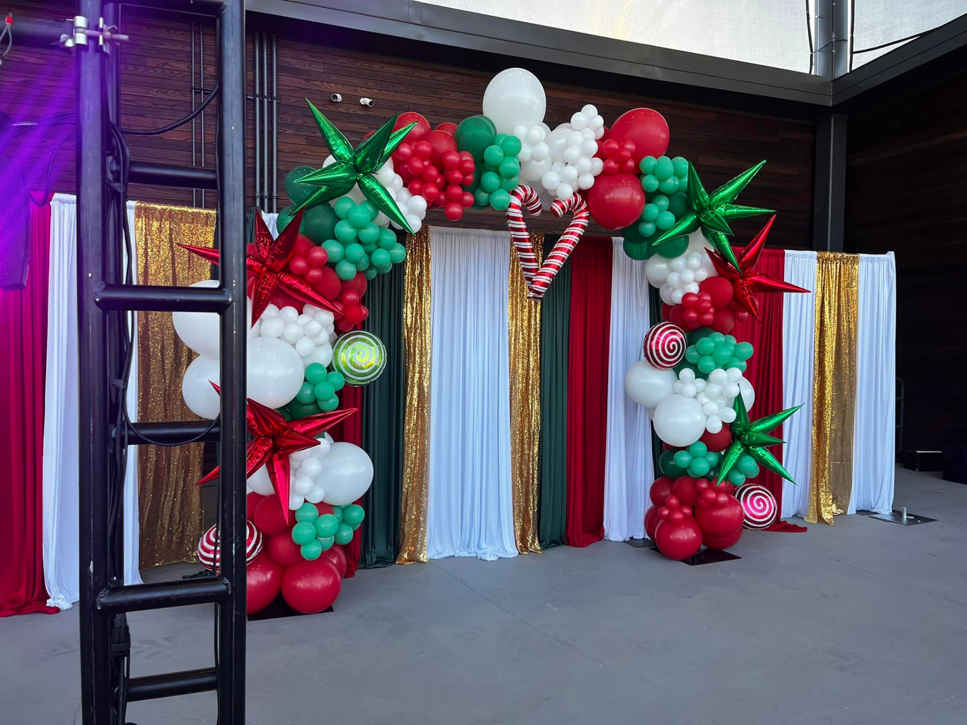 Red, green and white holiday balloon arch with candy accents and draped backdrop