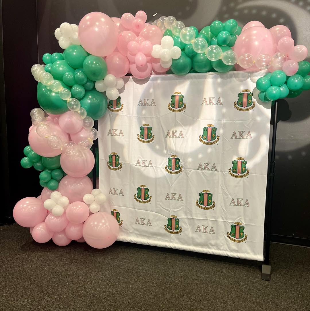 Pink, green and white balloon garland framing an AKA sorority branded step-and-repeat backdrop